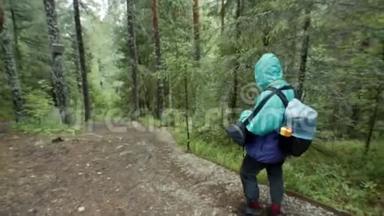 旅行者沿着森林小径漫步的后景。 <strong>库存</strong>录像。 带着背包和雨衣的旅行者走在崎岖的道路上